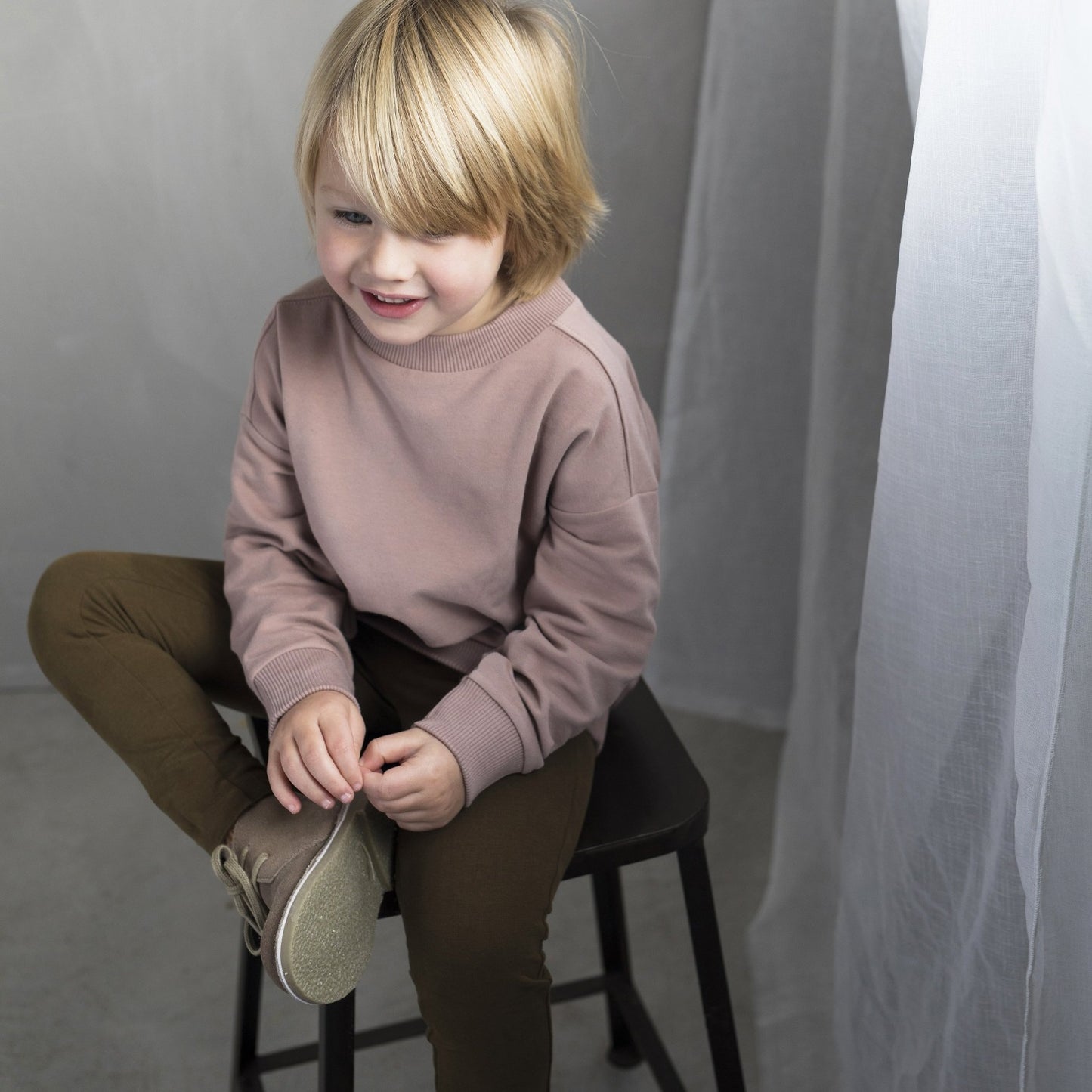 A little boy wearing the Oversized Sweater colour Powder by sustainable kidswear brand Phil&Phae